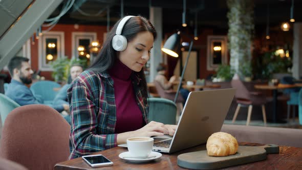 Female Freelancer Working with Laptop Typing and Enjoying Music with Headphones in Cafe