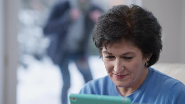 Closeup Portrait of Caucasian Woman Using Tablet and Noticing Masked Robber Behind Glass Door at