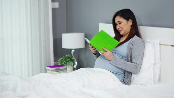 pregnant woman reading a book on a bed