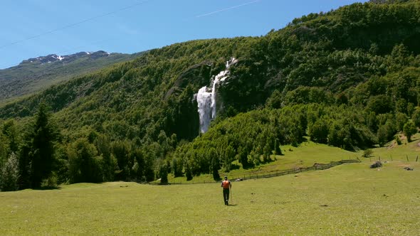 Man performs trekking in mountains with beautiful waterfalls in the background.