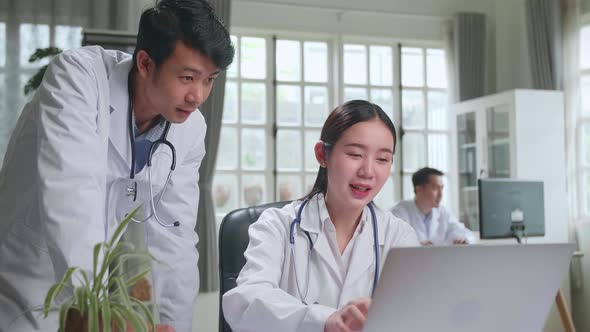 Two Asian Professional Physicians Talking, Consulting And Working On Laptop Computer