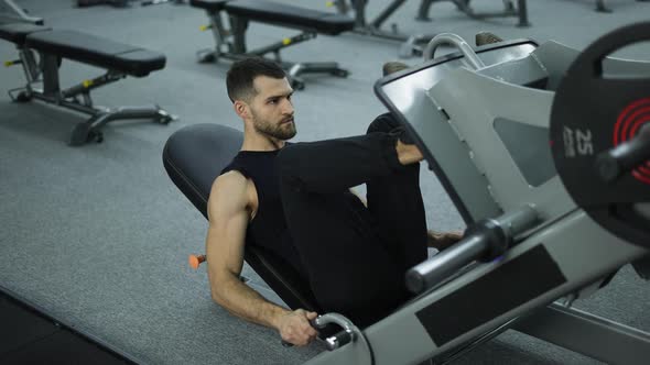 Muscular Man Exercises on a Sports Training Apparatus for Leg Muscles Lifting Weights