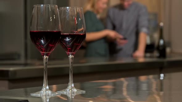 Wine Glasses on the Table, Couple Using Smart Phone Together at Home on the Back