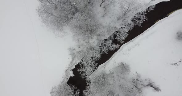 Flying Over Dark Black River and Snow Covered Land