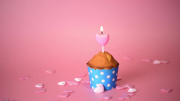  One cupcake or muffin with pink heart shape candle, flame blow out on a pink background