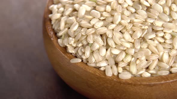 Full rustic wooden bowl of integral rice grains. Uncooked seeds. Macro