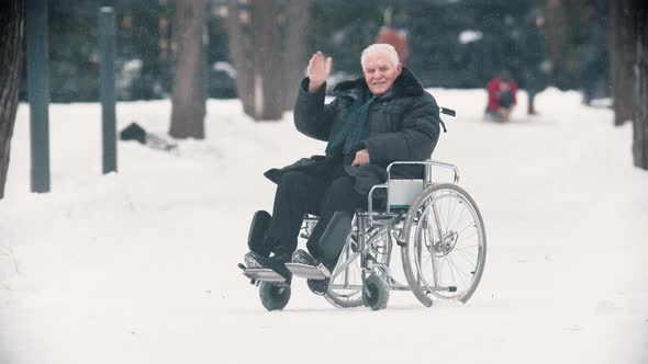 An Old Man Veteran Sitting in a Wheelchair and Waving with His Hand To the Camera