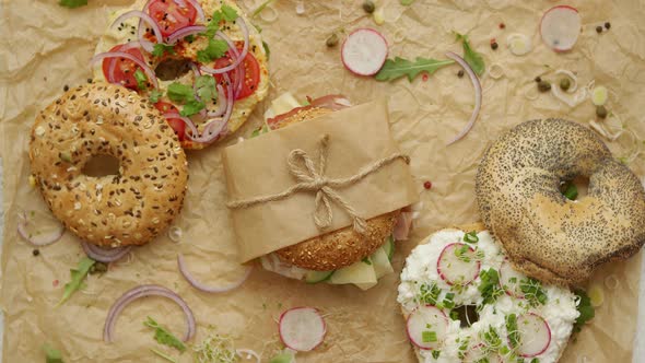 Bagels with Ham, Cream Cheese, Hummus, Radish Wrapped in Brown Baking Paper Ready for Take Away