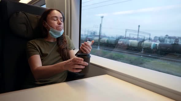 Portrait of an Adult Smart Woman in a Medical Mask Drinking Coffee and Typing Text Messages on the