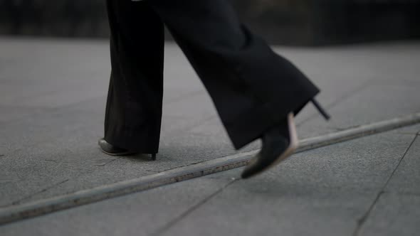 Women's Feet in Black Trousers and Highheeled Shoes Walk on the Pavement Tiles