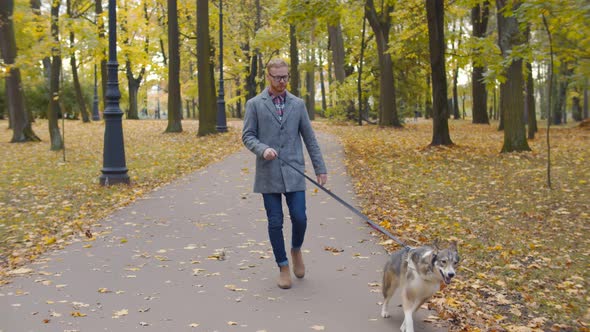 Young Hipster Man in Glasses Walking in Autumn Park with Dog