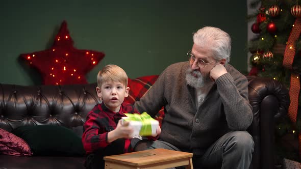 Little Boy in a Festive Red Plaid Shirt is Shake Gift Box in Anticipation of Surprise