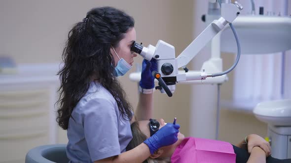 Side View Focused Professional Young Female Dentist Using Dental Endodontic Binocular Microscope