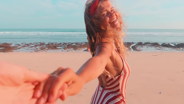 Young Caucasian Woman in Swimsuit Runs Along Beach Holding Person Hand