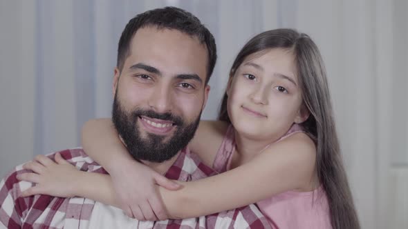 Close-up Portrait of Happy Middle Eastern Father and Daughter Smiling at Camera. Brown-eyed Man and