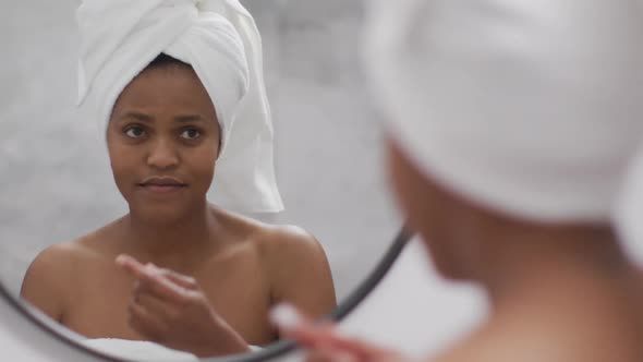 Happy african american woman apply cream on face in bathroom