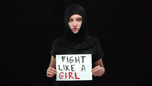 Muslim Woman in Hijab Posing with Fight Like a Girl Sign at Black Background