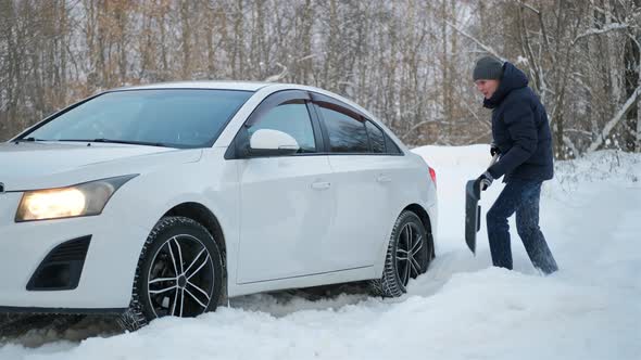 Man Digging Snow with Shovel Near Stuck Car