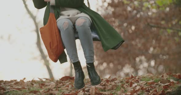 Young Woman Swinging in an Autumn Park. Colored Leaves on the Ground. Tree in Background. Slow