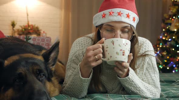 Pretty Woman in a Warm Knitted Sweater Drinks Hot Chocolate and Relaxes While Lying on the Bed with