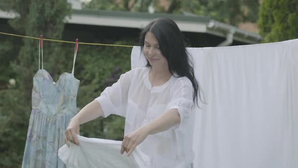 Attractive Senior Woman with Long Hair Black Hair Hanging White Clothes on a Clothesline Outdoors