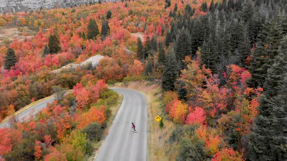 Aerial pan out shot of a man riding a longboard down Squaw Peak Road in Utah during autumn.