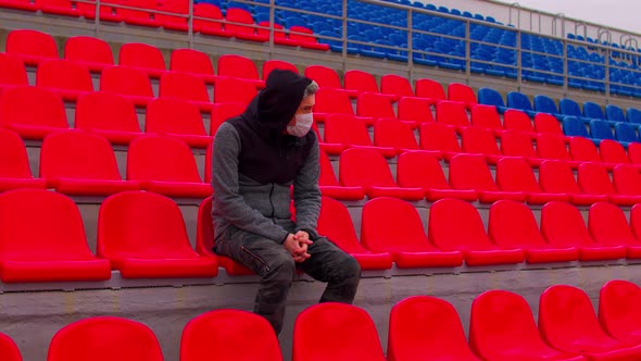 Young Man in Medical Mask Sitting on Stadium Bleachers Alone