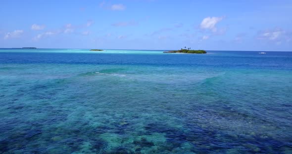 Wide flying tourism shot of a sandy white paradise beach and aqua blue ocean background in vibrant 