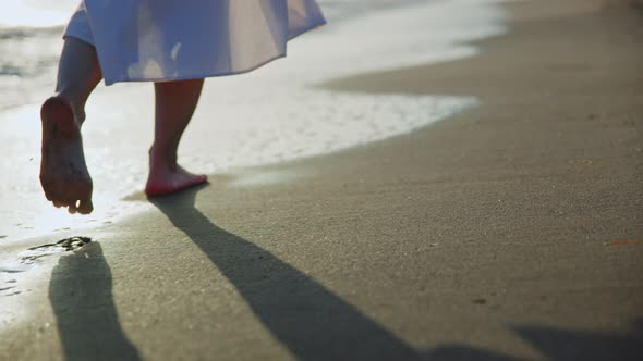 Barefoot woman walking on the beach at sunset, close-up