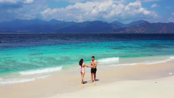 Guy and girl tanning on tranquil resort beach adventure by blue green water with white sandy backgro