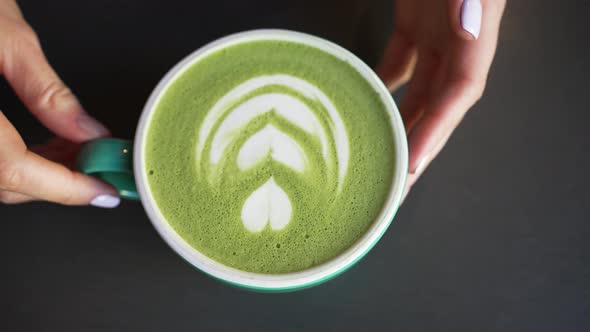Female Hands Put Cup of Green Matcha with Latte Art on Table