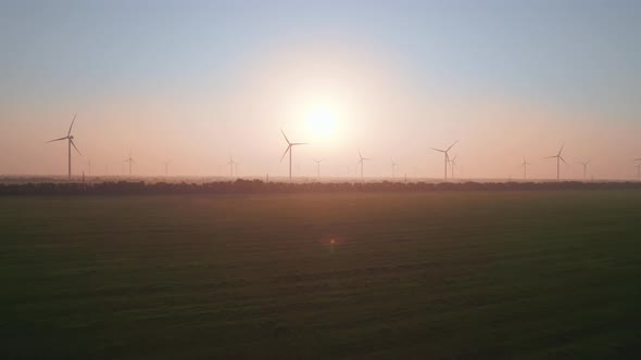 Windmills with rotating wings at sunset or sunrise.