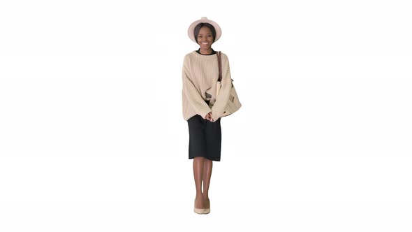 Smiling African American Woman in Knitwear and White Hat Posing While Walking on White Background