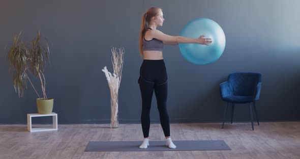 Young Sporty Woman Is Exercising By Doing Squats with Fitball at Hands in Training Gym