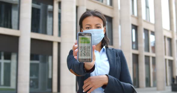 African Businesswoman in Safety Mask Showing Smartphone Screen with Online Vaccination Passport