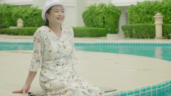 Happy senior woman relaxing sitting at poolside in hotel