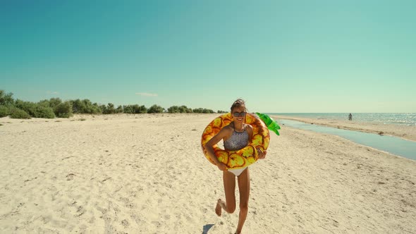 Young Happy Woman with Perfect Slim Tanned Body and Running on Empty Beach to Water Holding Giant