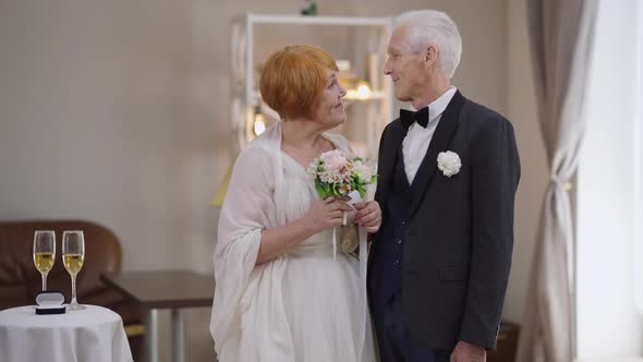 Portrait of Loving Smiling Senior Groom and Bride Putting Heads Together Looking at Camera Standing