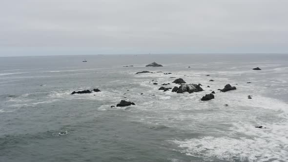 Drone aerial over choppy ocean waves toward a fishing boat in the distance on a cloudy day, Pacific