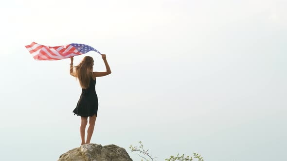 Young happy american woman with long hair raising up waving on wind USA national flag