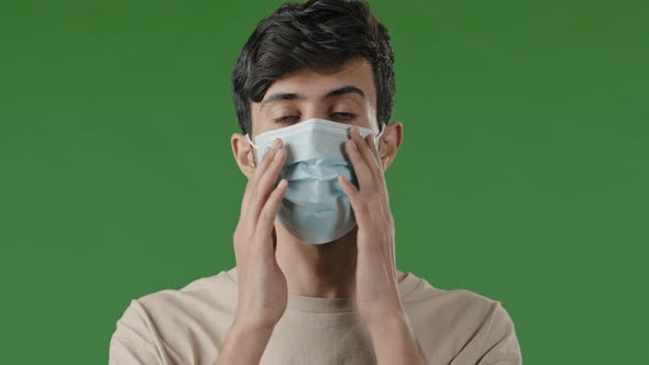 Close Up Serious Young Arab Guy Putting on Medical Mask Standing in Studio on Green Background