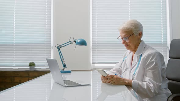 Smiling mature female doctor with spectacles writes message