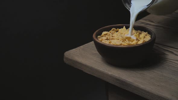 Milk is Poured Into a Bowl with Cornflakes on a Wooden Table