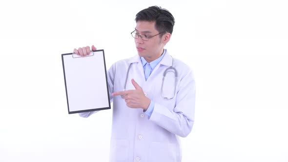Stressed Young Asian Man Doctor Showing Clipboard and Giving Thumbs Down