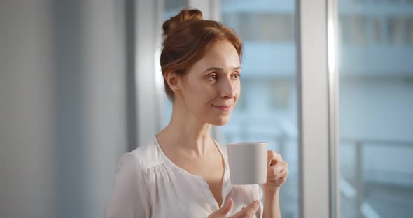 Businesswoman in Corporate Workplace Taking Break and Drinking Coffee While Standing Near Window