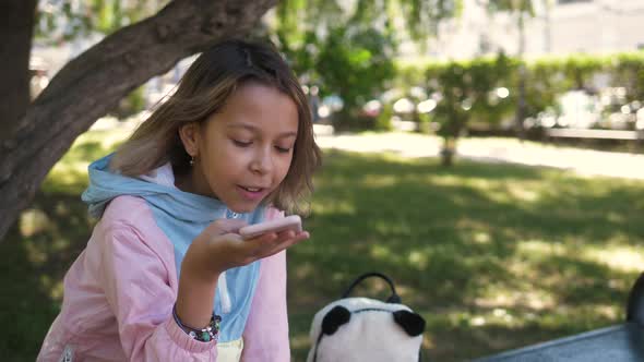 Little Girl Child Kid Sitting on Grass in Park Audio Message on Phone, Voice Recognition