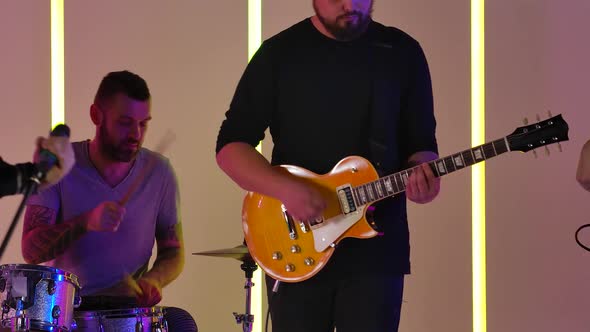 The Band Performs Their Music in the Studio Against the Backdrop of Multicolored Neon Lights