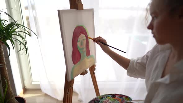 Girl Sits on a Chair Near the Easel and Holds a Palette and a Brush in Her Hands