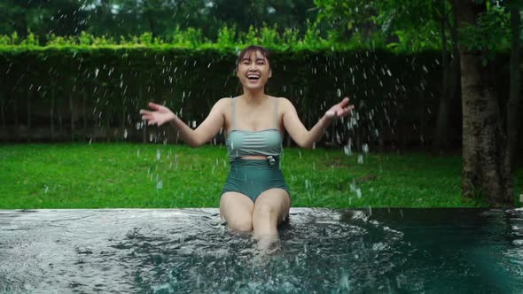 slow-motion of woman sitting on edge of swimming pool and playing water splashing