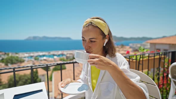 Pleased Woman Enjoying Morning Coffee While Sitting on Terrace with Sea View on Turkish Resort Using